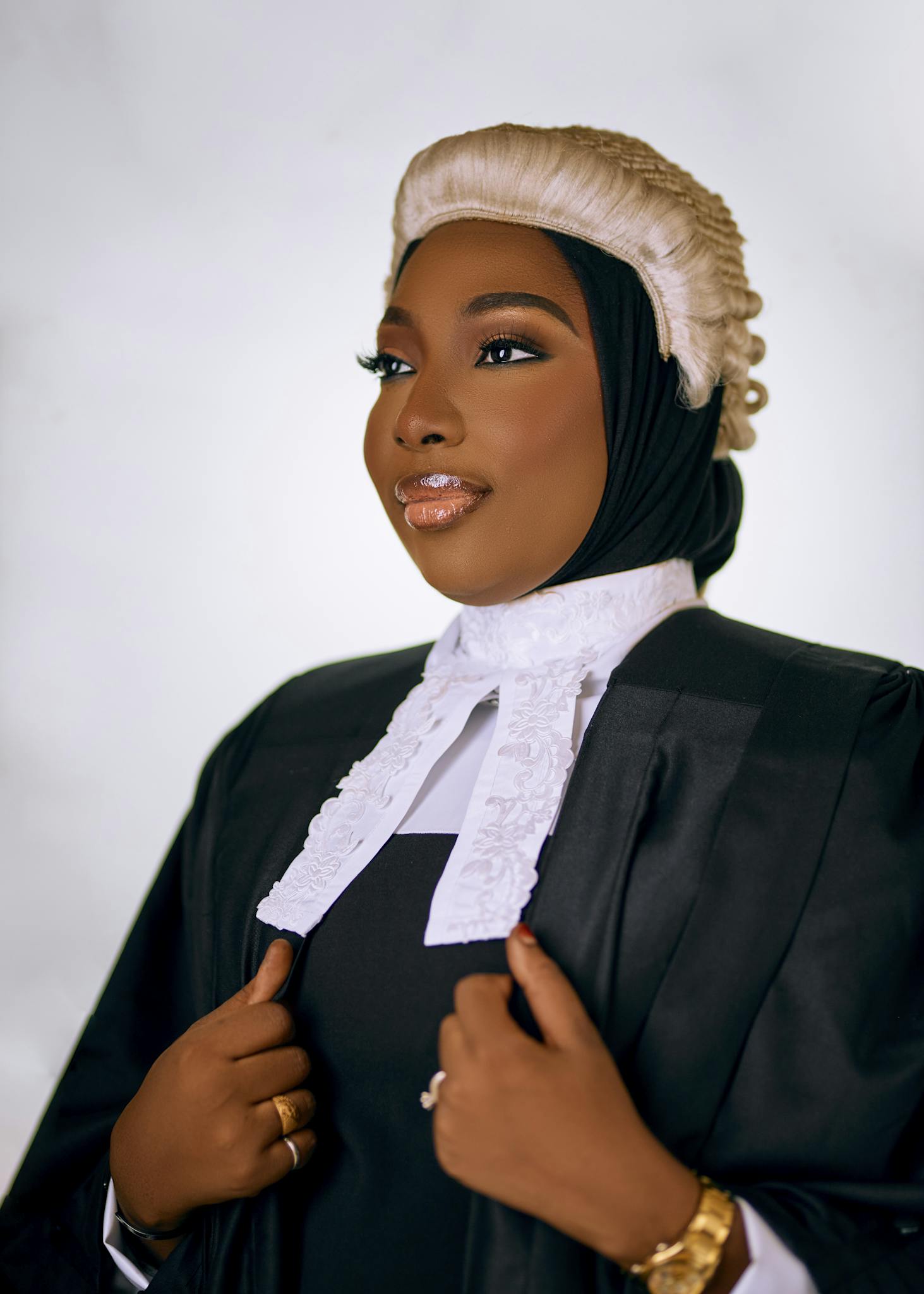 Portrait of a confident female lawyer in formal attire and traditional barrister wig against a neutral background.